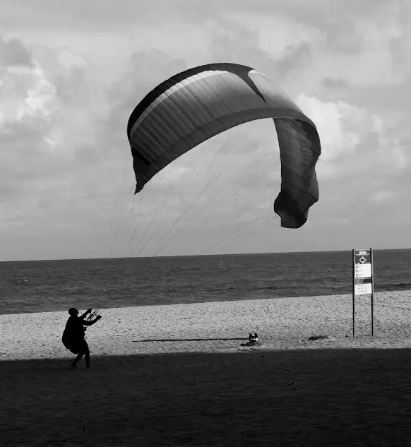 Pessoa soltando uma pipa em forma de parapente na Praia de Boa Viagem, em preto e branco